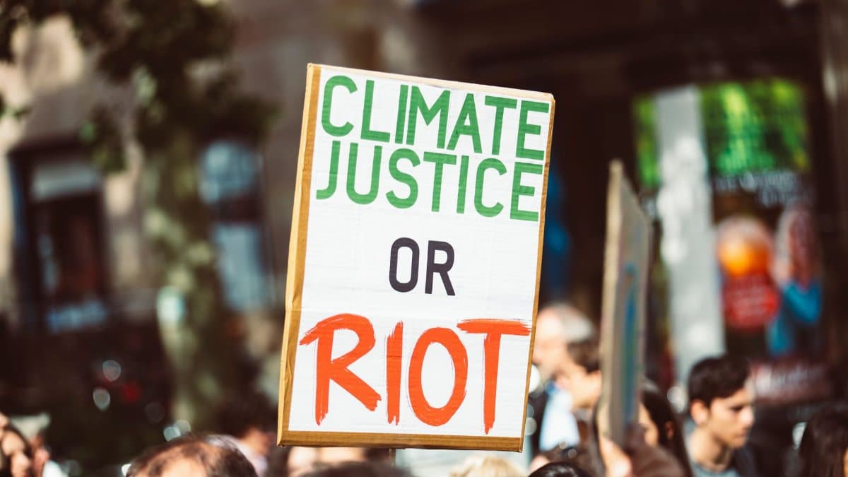 Close-up of a protest sign reading 'Climate Justice or Riot' in a street rally focused on climate change.