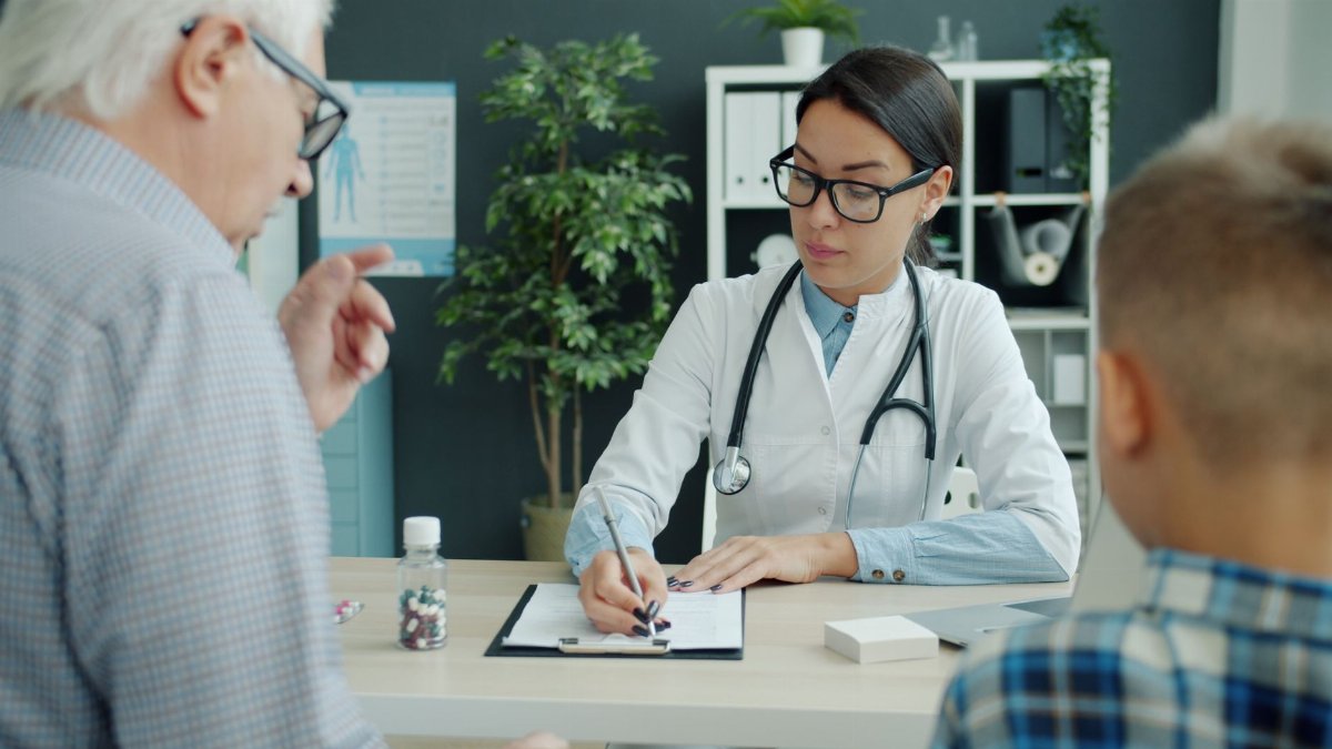 A doctor in an office consulting with an elderly man and a child, taking notes.