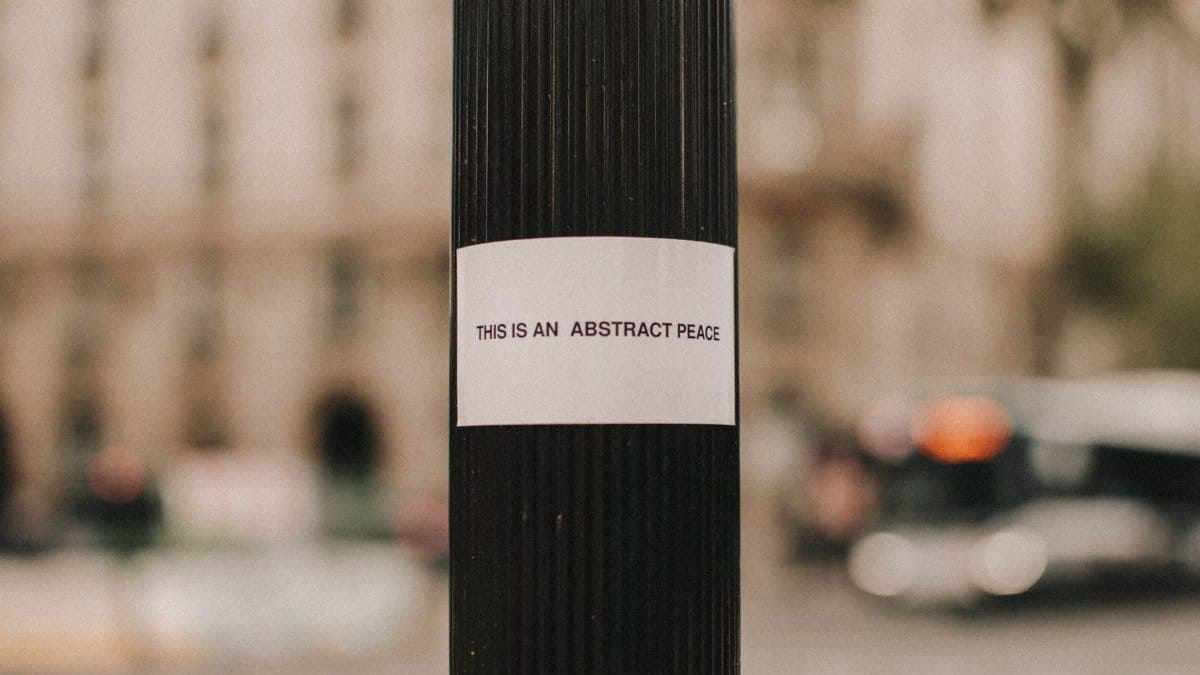 Close-up of a street pole with an 'abstract peace' message, in an urban setting with a blurry backdrop.