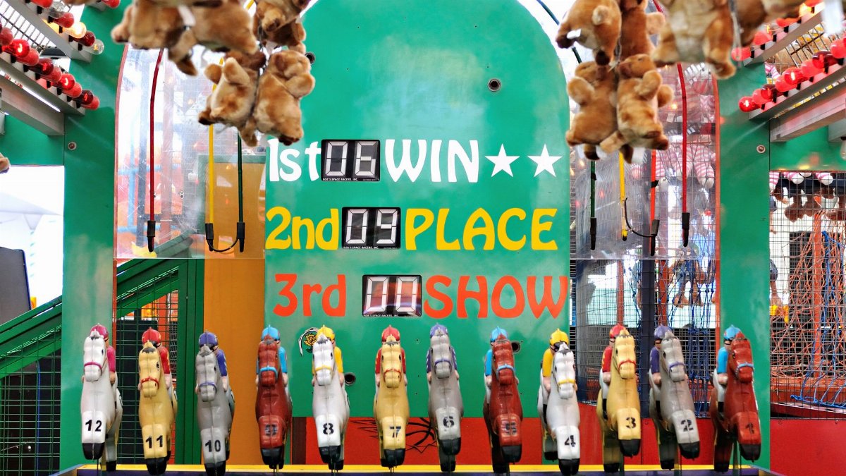 Vibrant carnival game featuring a toy horse racing setup with colorful displays and stuffed animal prizes.
