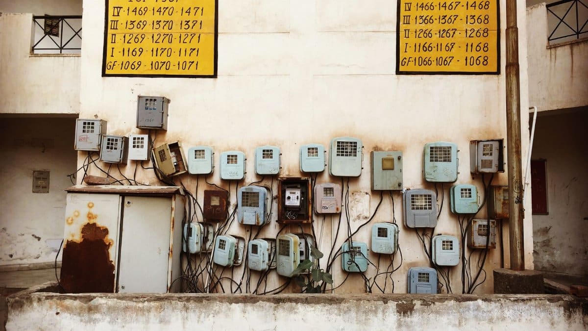 Aged electrical meters and wiring mounted on a concrete wall of an old building in India.