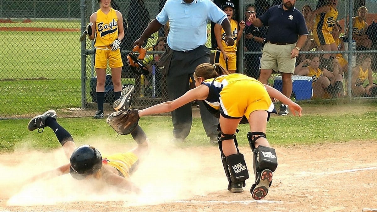 Youth softball player slides into home plate as the catcher attempts to tag. Sports action captured vividly.