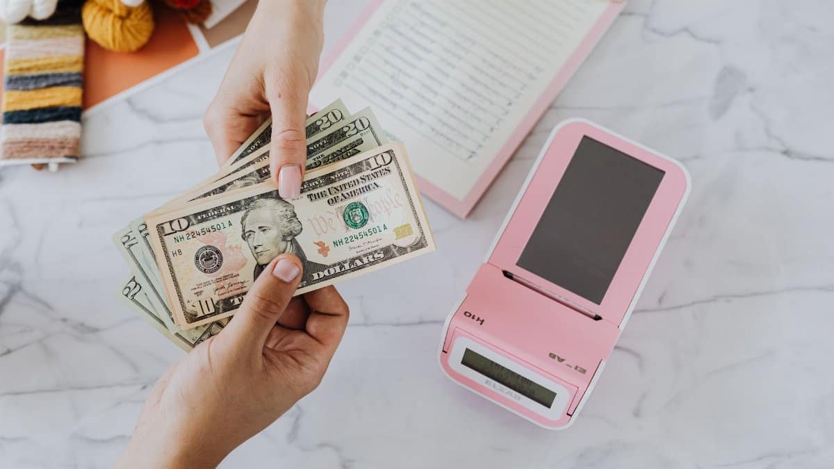 Close-up of hands exchanging US dollars with a pink calculator on a marble surface.