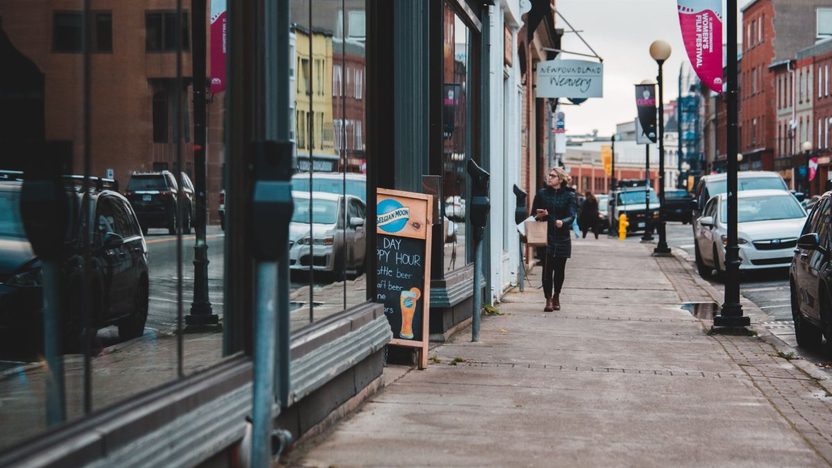 City street with reflections in storefront windows, featuring pedestrians and cars.