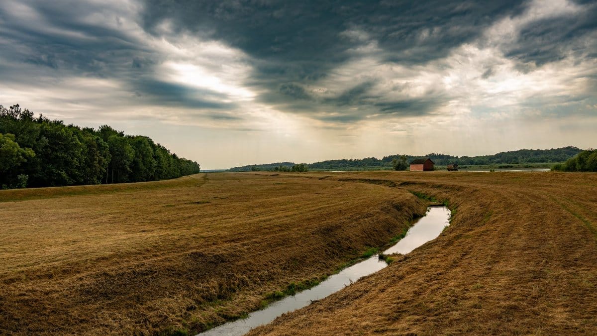 Beautiful rural landscape in Garešnica, Croatia, featuring green fields, a meandering stream, and dramatic clouds.