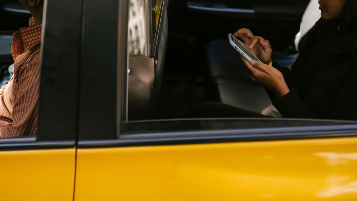 Side view of unrecognizable passenger browsing smartphone while sitting on backseat of yellow cab with anonymous driver during ride