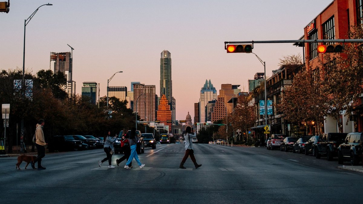 People crossing a city street in Austin, Texas at sunset with the skyline in the background.