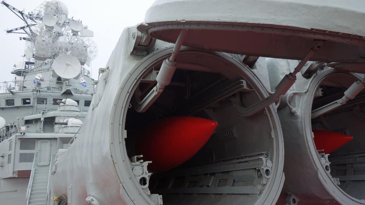 A detailed view of a naval warship's open missile launcher bays showing red missiles inside.