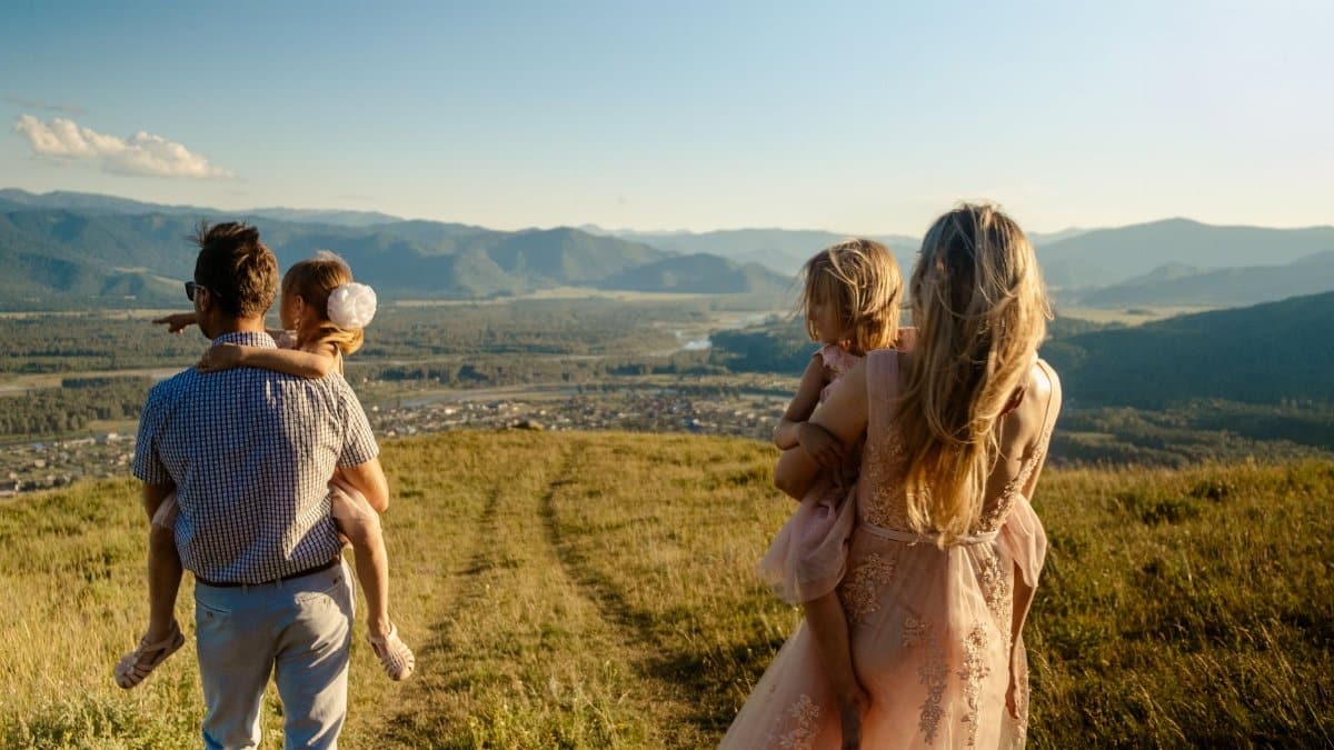 A family enjoying the outdoors with children on a hill, overlooking a valley on a sunny day.