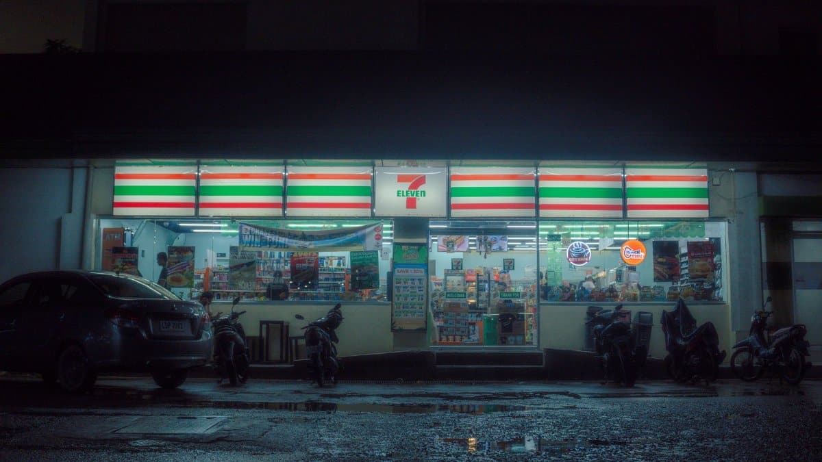 Moody nighttime scene of a 7-Eleven store with parked vehicles and reflections.