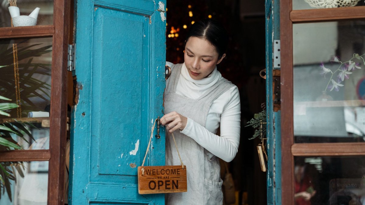 A woman adjusts an open sign on a blue wooden door of a cafe inviting customers inside.