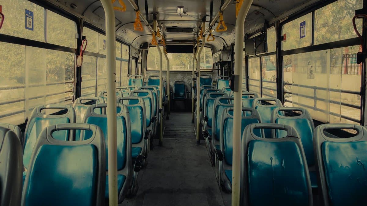 View of an empty public bus interior with blue seats and yellow handrails.