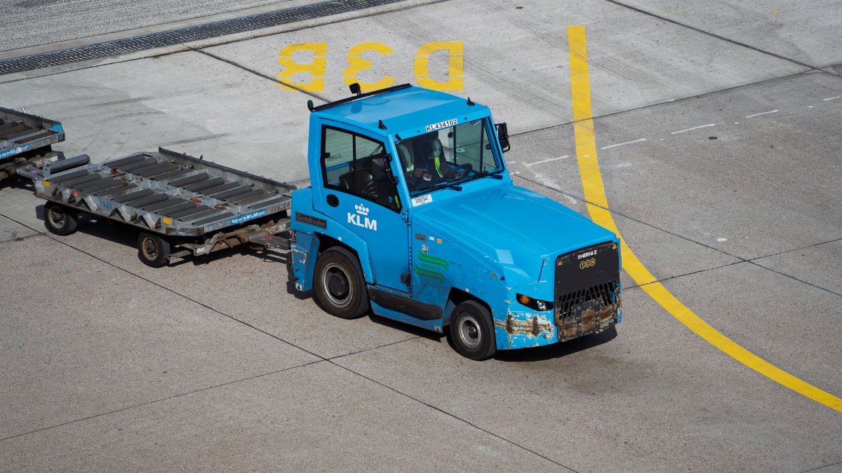 KLM Ground Support Equipment towing baggage carts on airport tarmac.