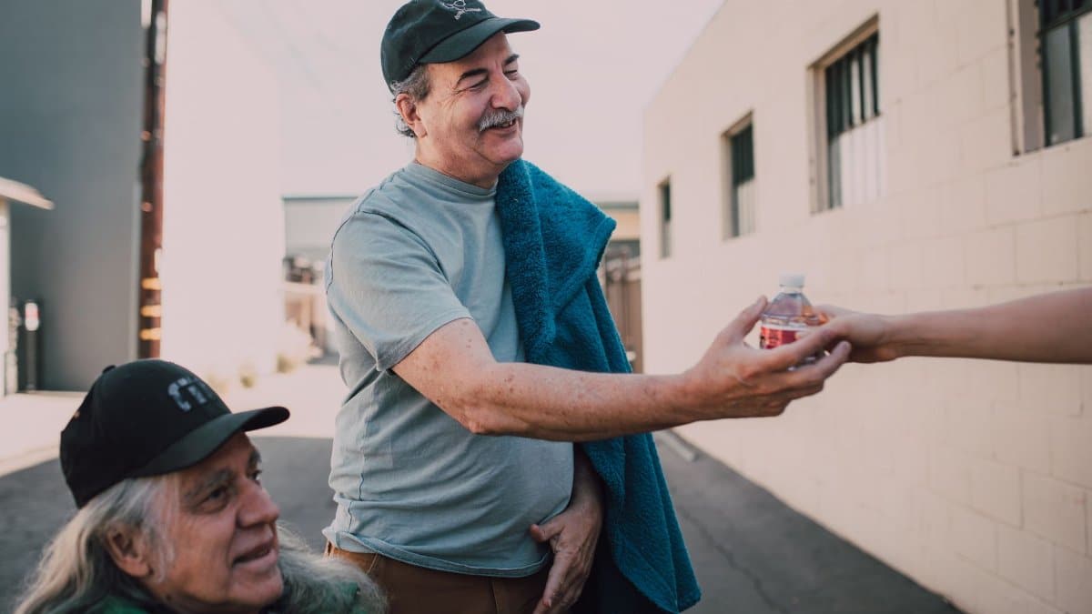 Two adults exchanging bottled water with kindness in an urban setting.