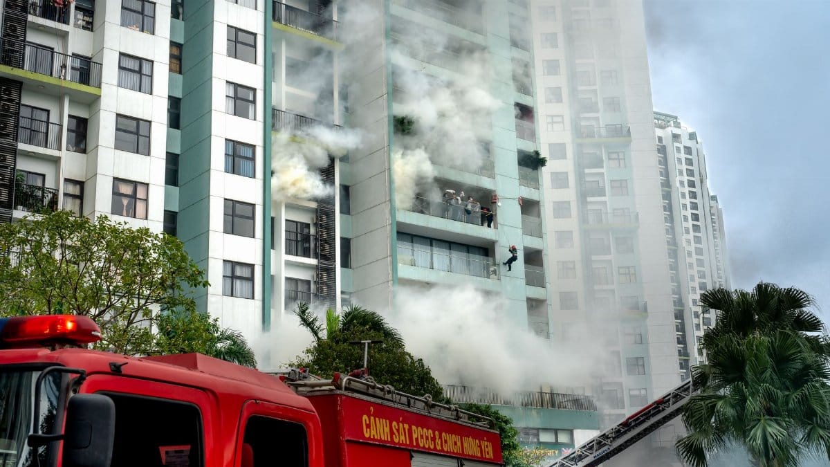 Firefighters respond to a building fire with smoke and emergency vehicles in an urban area.