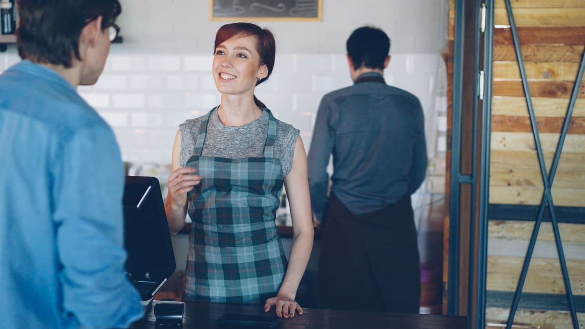 Smiling barista at the counter engaging with a customer in a cozy café.