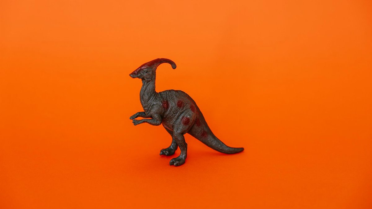 Miniature dinosaur figurine on a bright orange backdrop, perfect for creative projects.