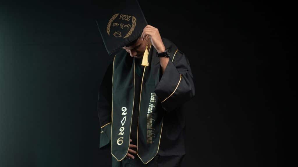 A graduate wearing a cap and gown, class of 2026, looking down in a studio setting.