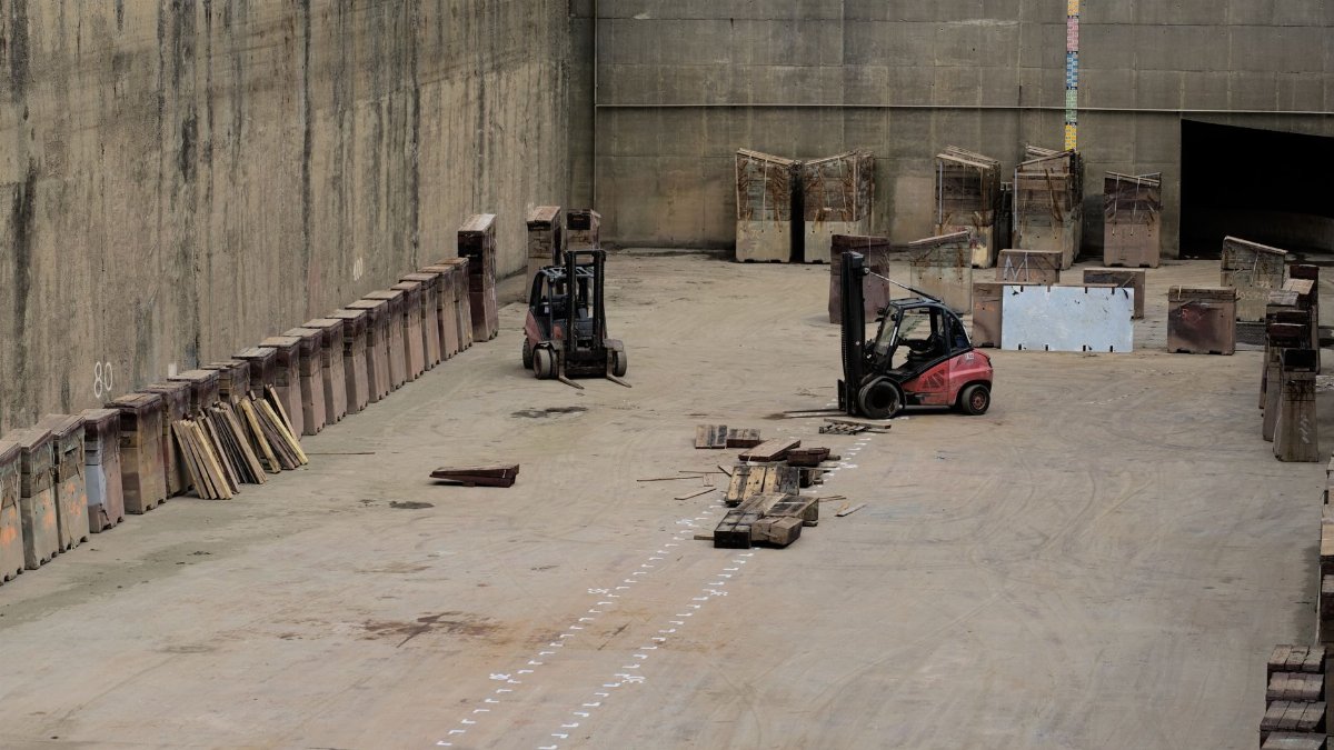 Two forklifts in a large industrial warehouse setting with stored machinery.
