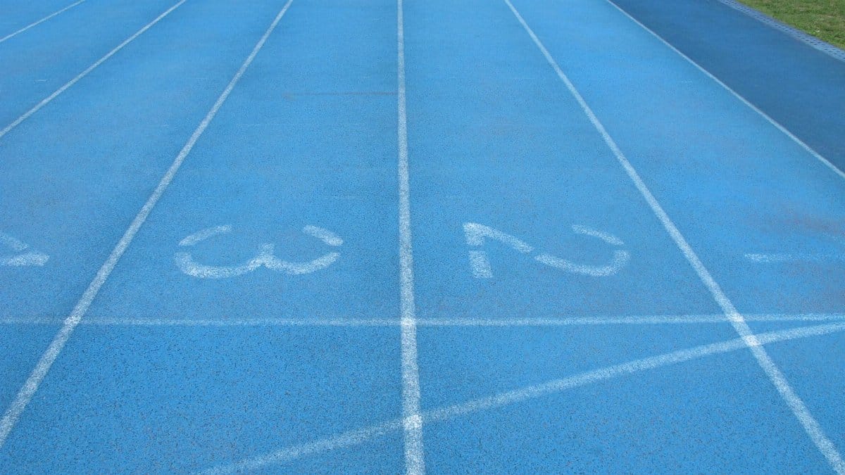 Close-up view of a blue athletics track with white lane numbers and markings.