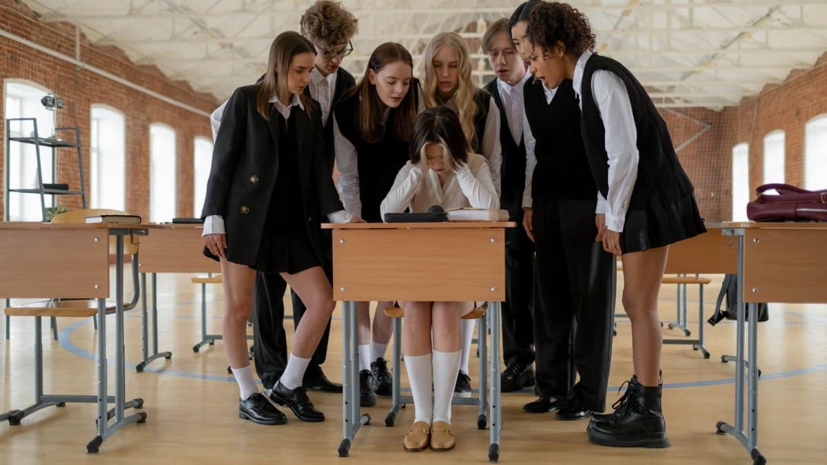 A diverse group of students surrounds a lone student in a modern classroom setting.