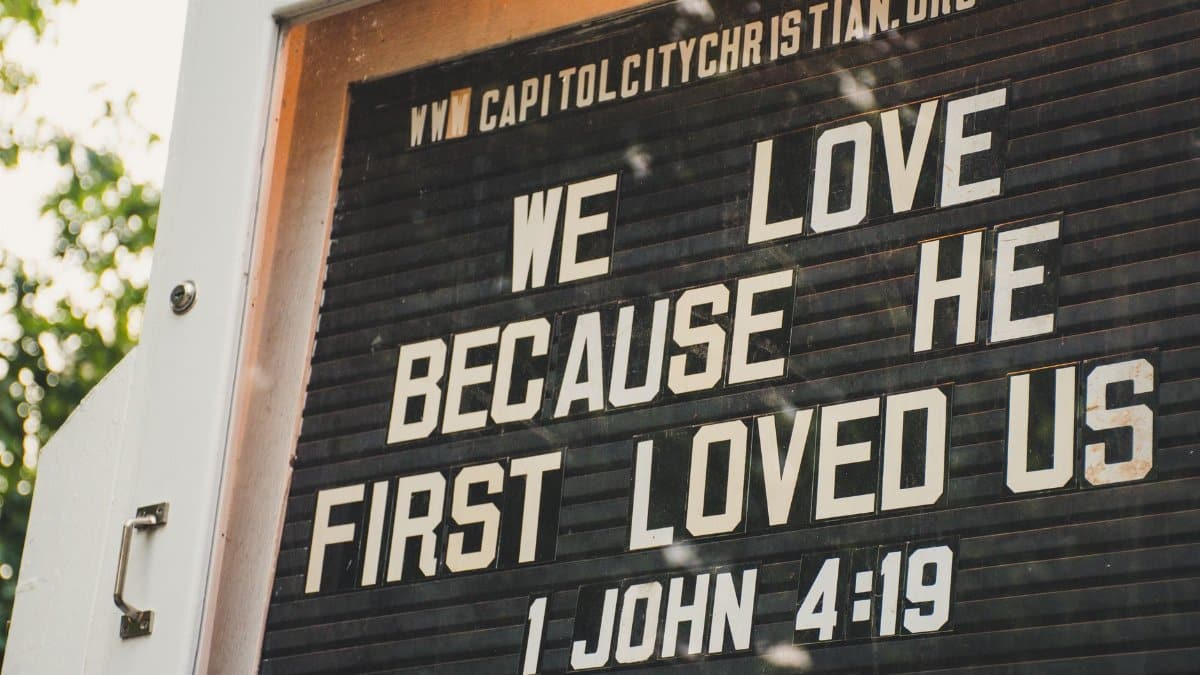 Church sign displaying biblical verse about love from 1 John 4:19 in outdoor setting.