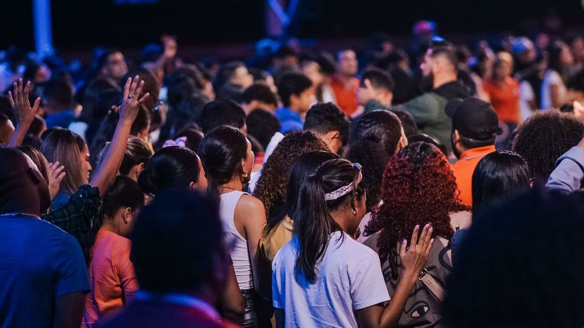 Back view of a large congregation standing in worship, raising hands in unity and spirituality.