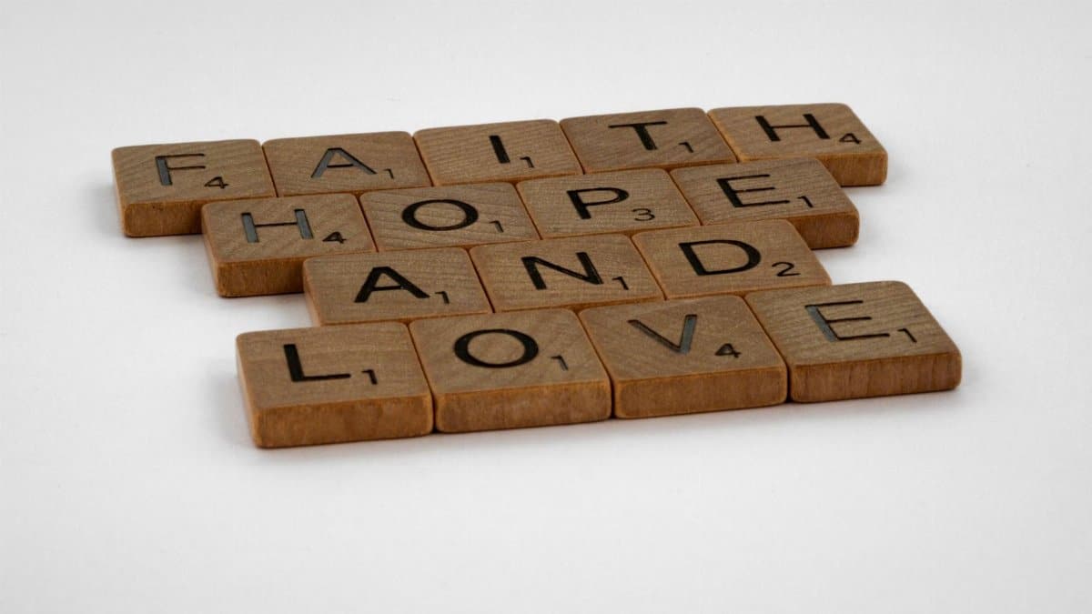Wooden Scrabble tiles arranged to spell Faith, Hope, and Love against a white background.