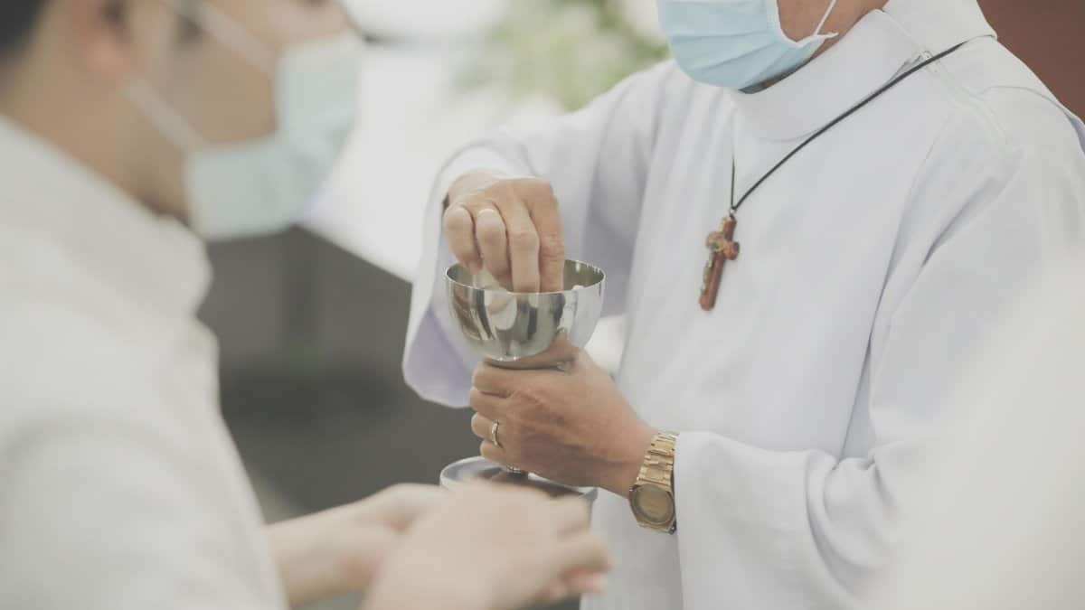 A priest wearing a face mask giving communion to a parishioner during a religious service.