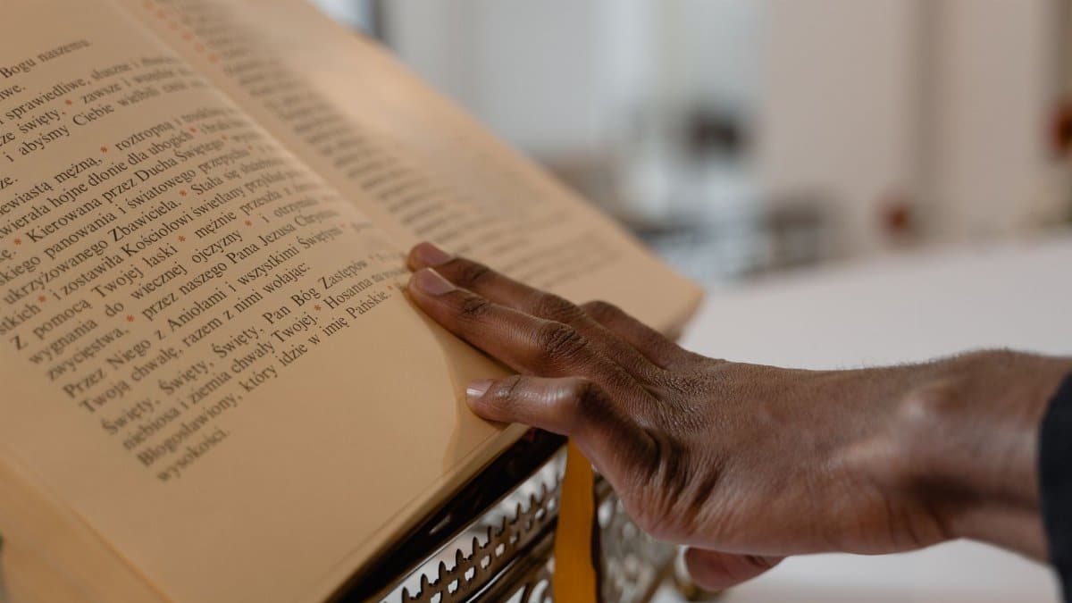 Close-up of a hand touching a religious text on a stand, symbolizing faith and spirituality.