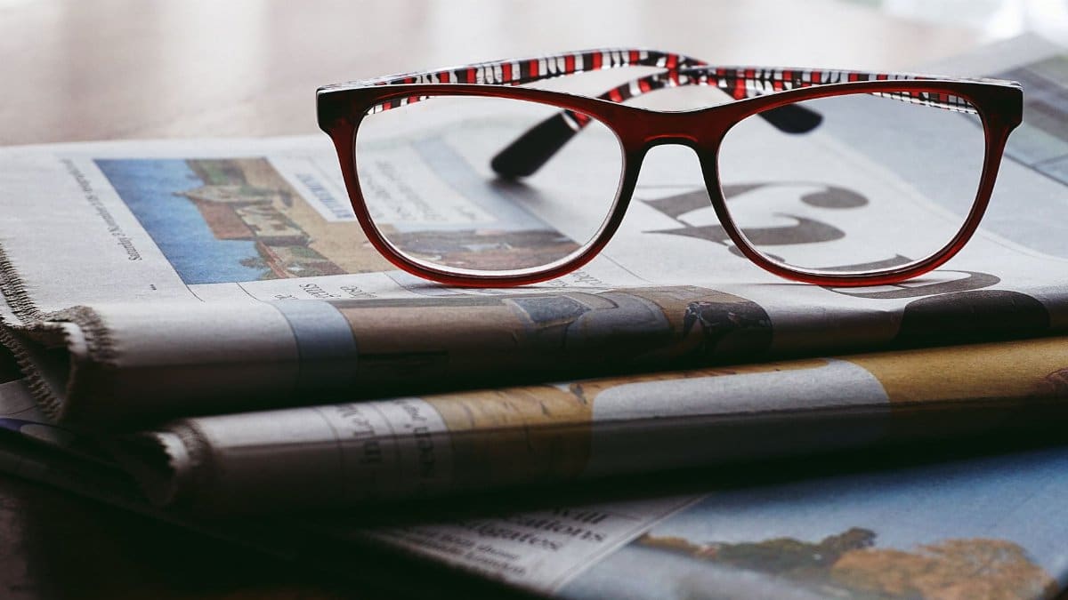 Close-up of reading glasses resting on a stack of newspapers, symbolizing knowledge and study.