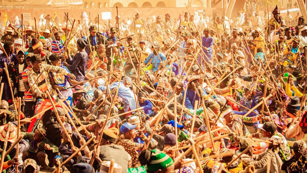 A vibrant outdoor scene of a traditional stick fighting ceremony with a large crowd participating energetically.