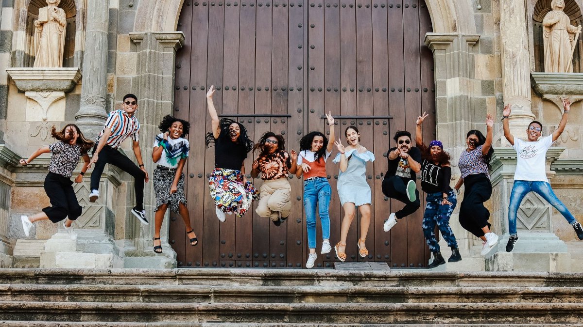 A lively group of friends joyfully jumping on steps outside a historic cathedral.