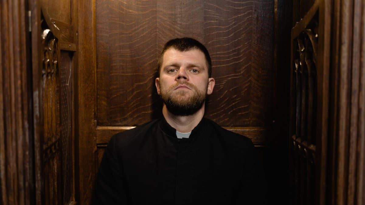 A priest sits solemnly in a classic wooden confessional, embodying faith and tradition.