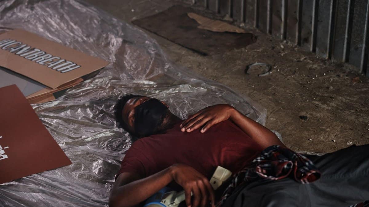 A man in a red shirt and face mask rests on the ground, symbolizing pandemic fatigue.