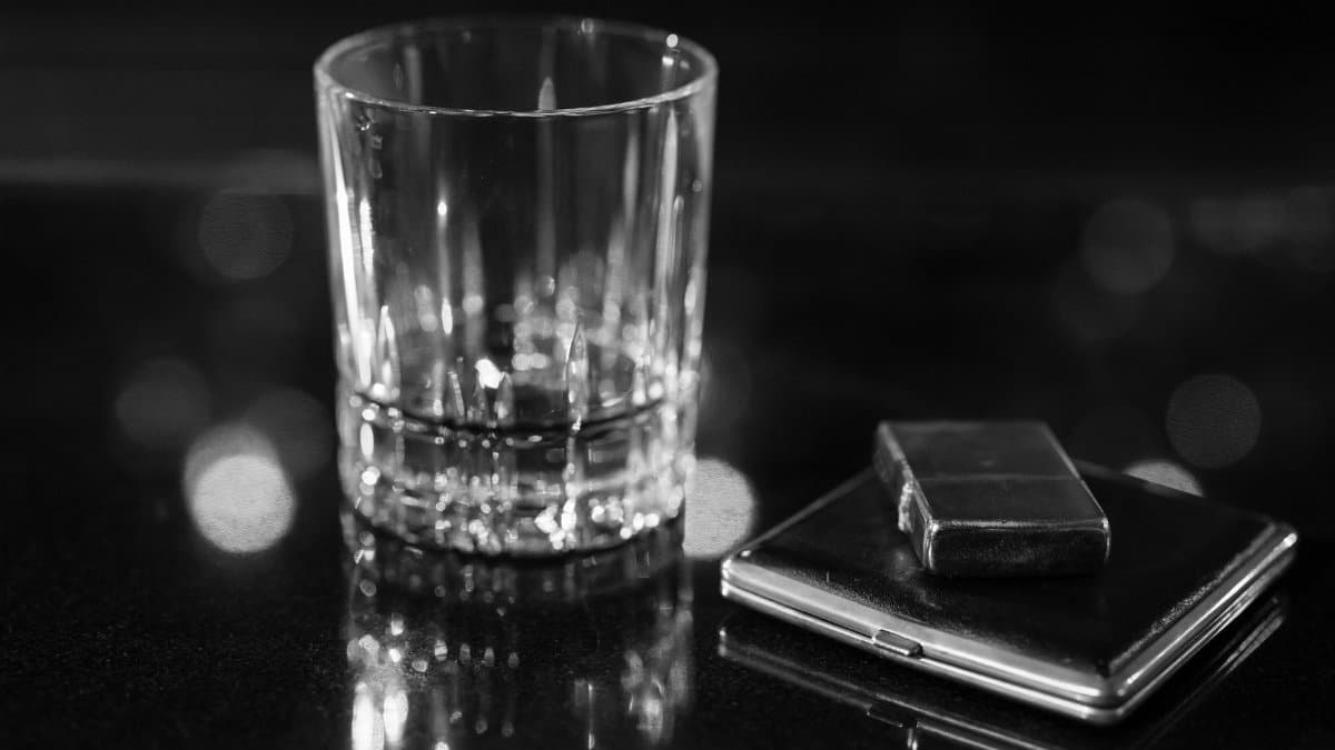 Monochrome image showing a glass and lighter on a reflective surface, perfect for bar themes.
