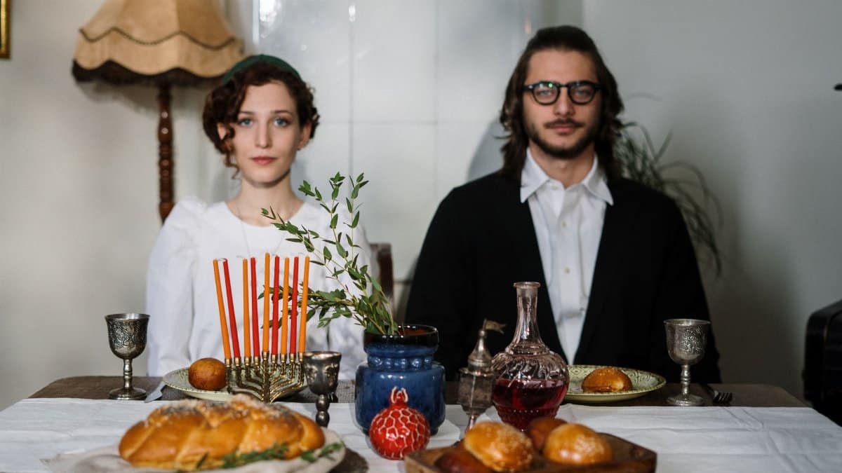 A Jewish couple celebrates Shabbat with traditional food and menorah at home.