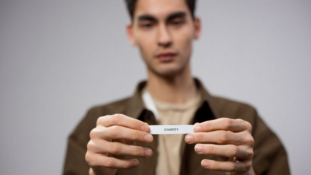 A man holds a note reading 'charity,' with the focus on his hands, expressing a charitable theme.