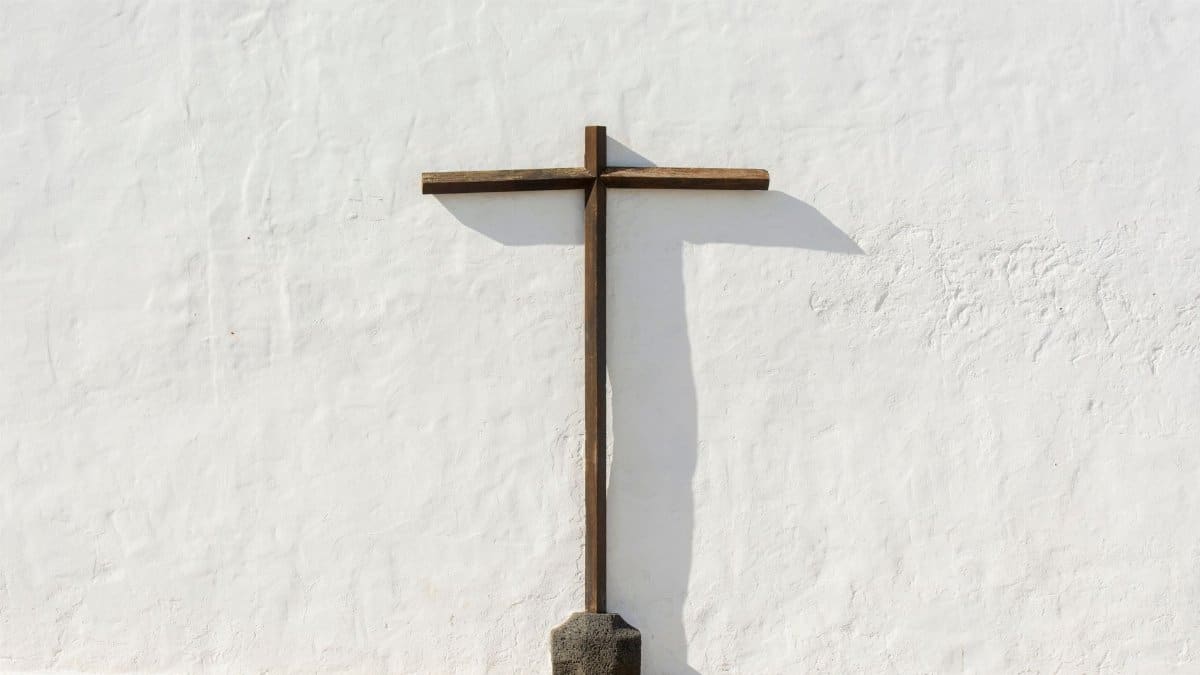 A simple wooden cross standing against a stark white wall, symbolizing faith and tranquility.