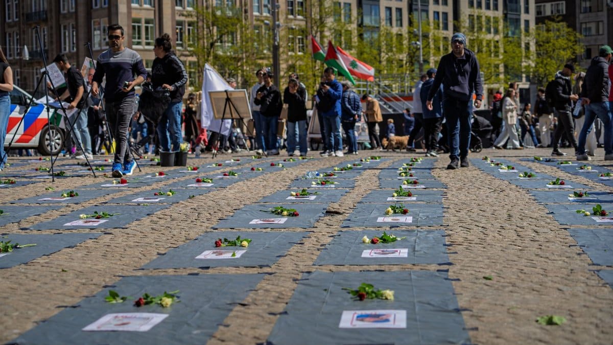 Public memorial event with flowers on display, and people gathered around in a public square.