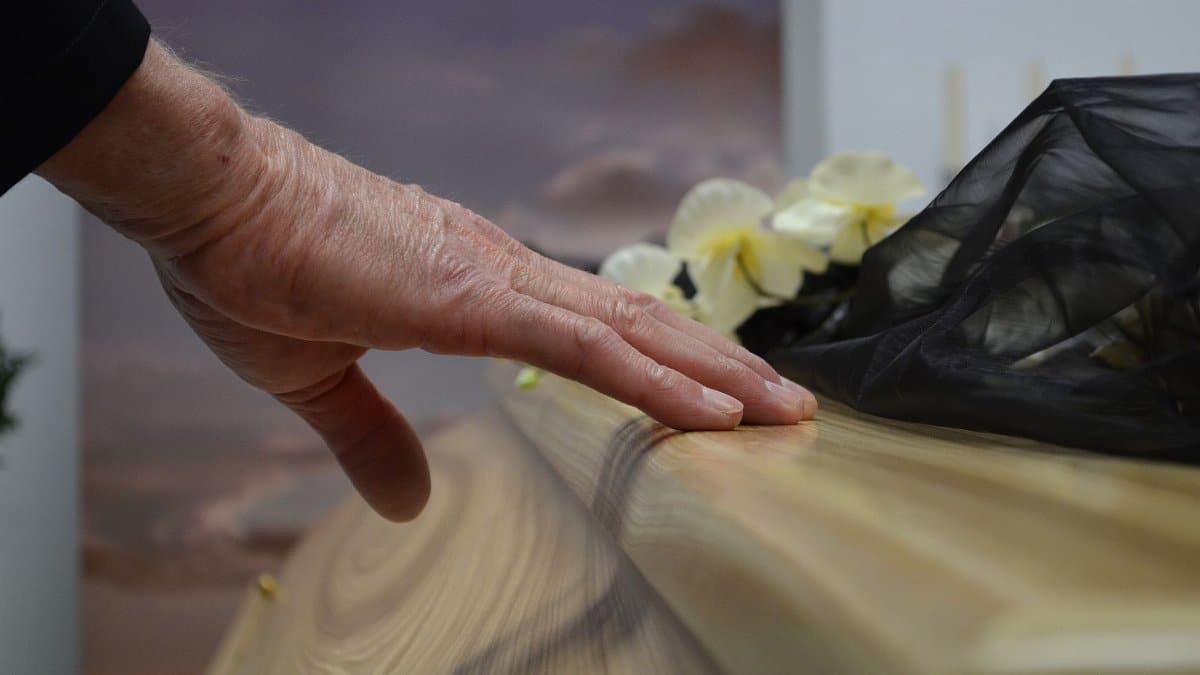 A touching moment of grief as a hand rests on a coffin, symbolizing loss and mourning.