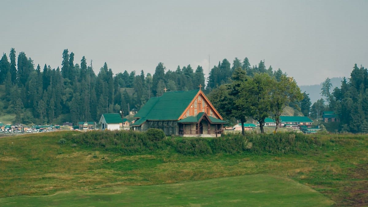 A picturesque rural church surrounded by lush greenery and forested hills.