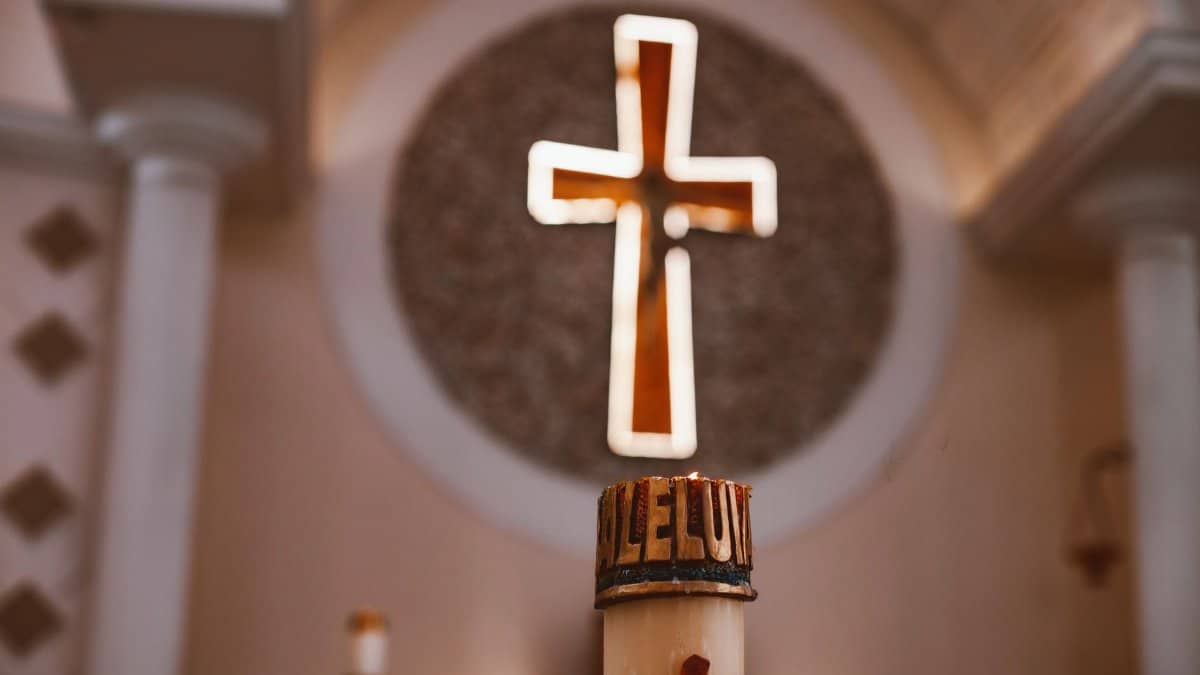 A glowing cross above an 'Alleluia' candle in a church, symbolizing faith and worship.