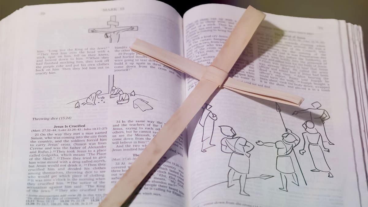 Bible open to crucifixion passage with wooden cross placed on top, symbolizing Christian faith.