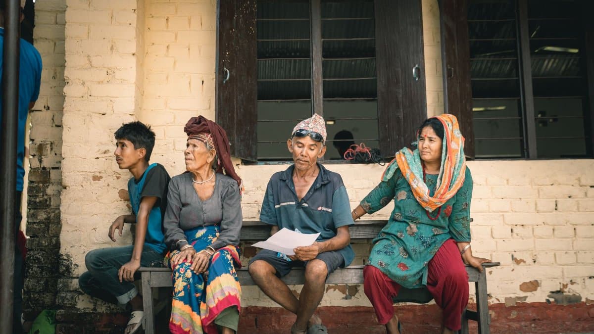 A South Asian family wearing traditional clothing seated on a bench outside.