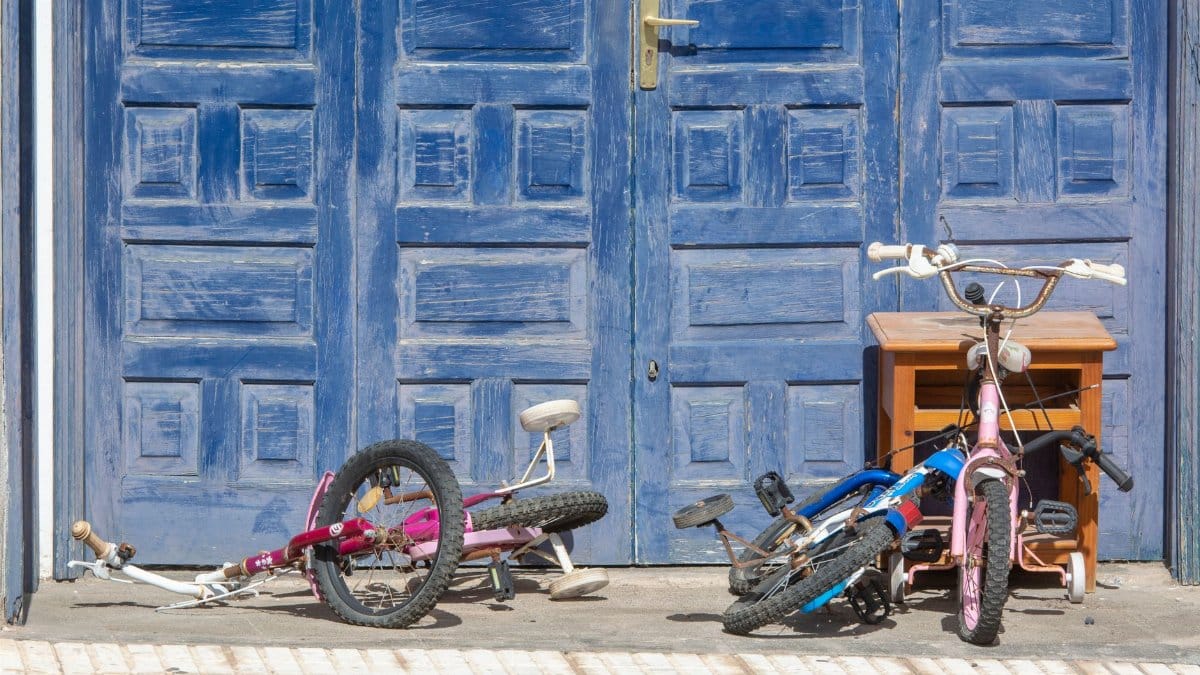 Two children's bicycles in front of a blue wooden garage door on a sunny day.