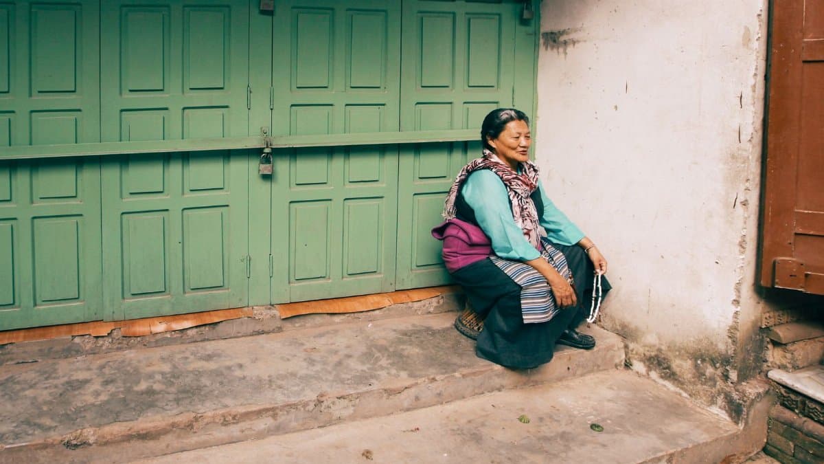 A senior woman sitting thoughtfully on stone steps near a closed green doorway.