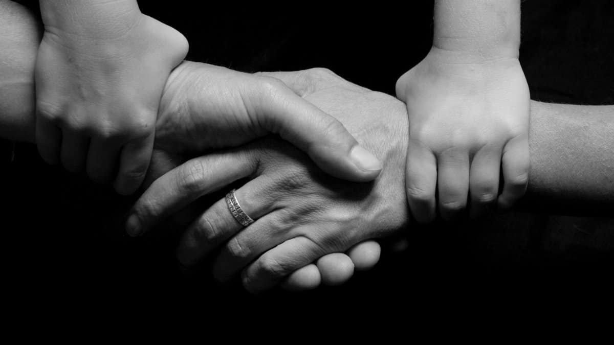 Monochrome image of a child's and adult's hands clasped together symbolizing trust and connection.