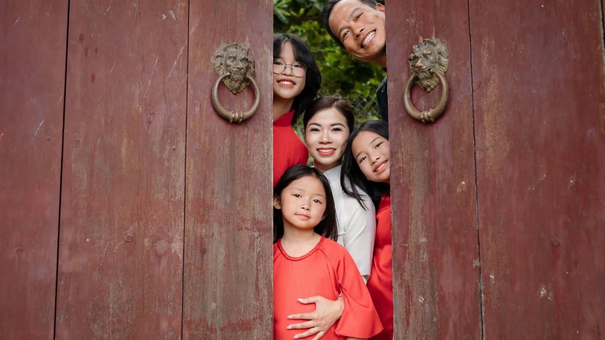 Happy family posing behind a wooden door amid greenery in Hội An, Vietnam.