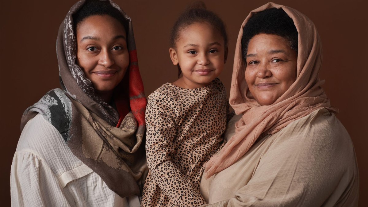 Three generations of women smiling warmly indoors, showcasing family and cultural unity.